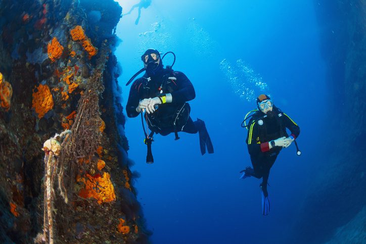 Underwater photo,  orange sponge and  old fishing net on colorful reef.  Scuba diving team, two scuba diver mid adult women and mature men in the blue  background. Exploring and enjoying Beautiful Sea Life.  Underwater scene at clear mediterranean sea.  Scuba diver point of view. Greece Europe.